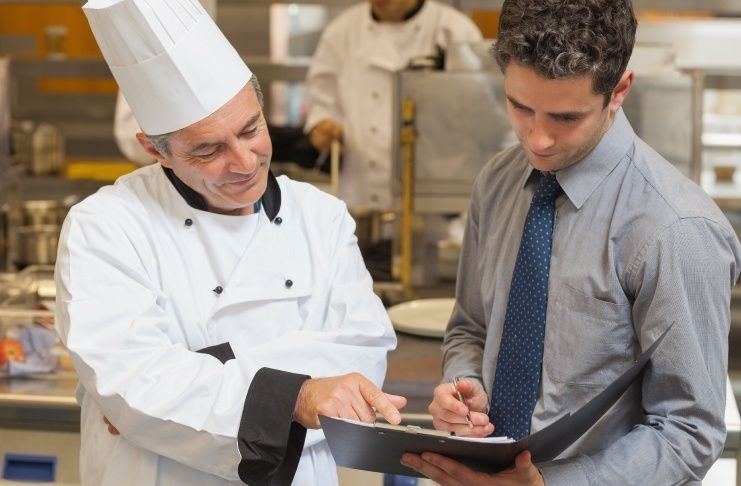Chef and manager reviewing figures on a clipboard in a restaurant kitchen